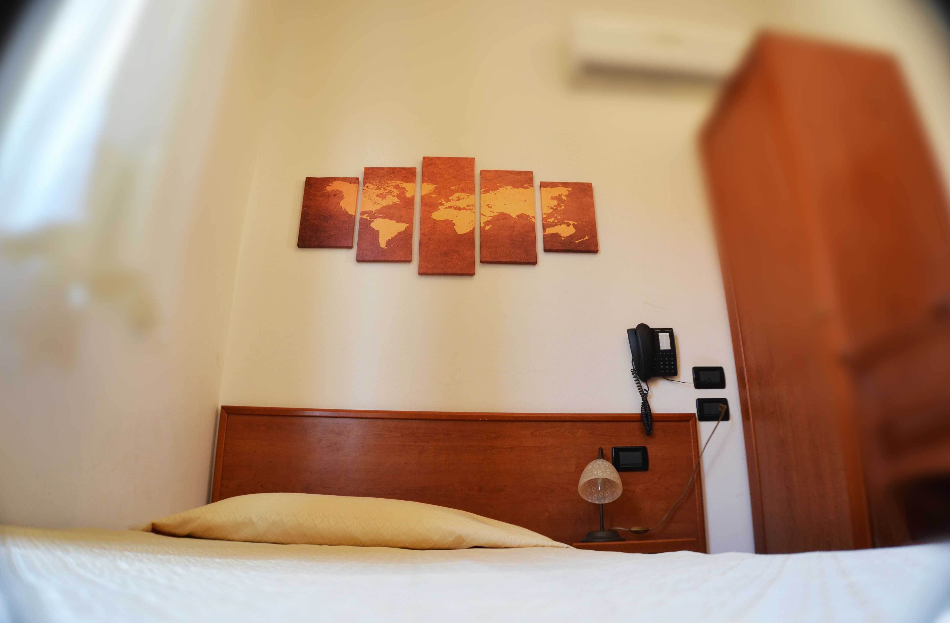 A hotel room with a wooden headboard, a bed with white bedding, a bedside lamp, a phone, and a wall-mounted artwork.