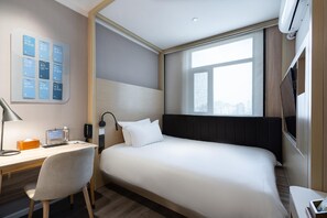 Habitación de hotel con cama, escritorio, silla y televisor montado en la pared.