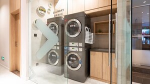 A modern laundromat with multiple washing machines and dryers, glass doors, and wooden cabinetry.