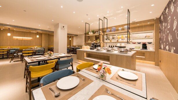 A modern restaurant with wooden paneling, a central island with kitchen appliances, and a variety of seating options including tables and chairs.