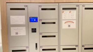 A row of metallic lockers with numbered compartments, a digital display, and QR codes.