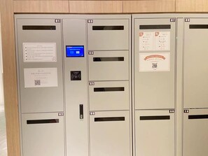 Una hilera de taquillas metálicas con compartimentos numerados, una pantalla digital y códigos QR.