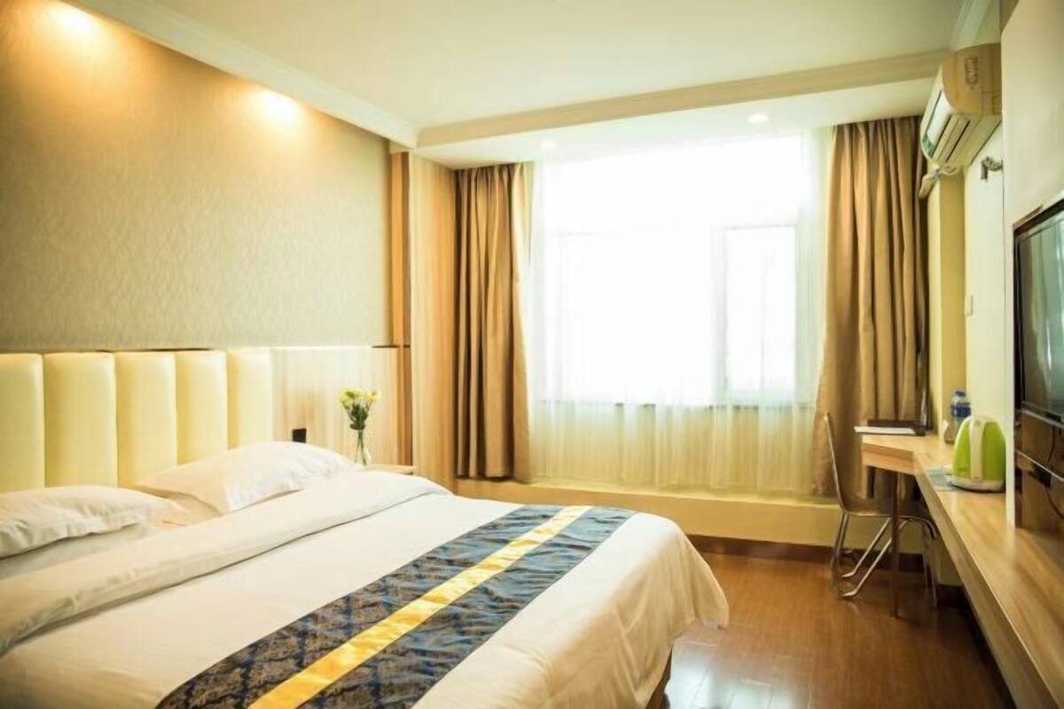 Une chambre d’hôtel avec un grand lit, un bureau avec une chaise, une télévision et une fenêtre avec des rideaux.