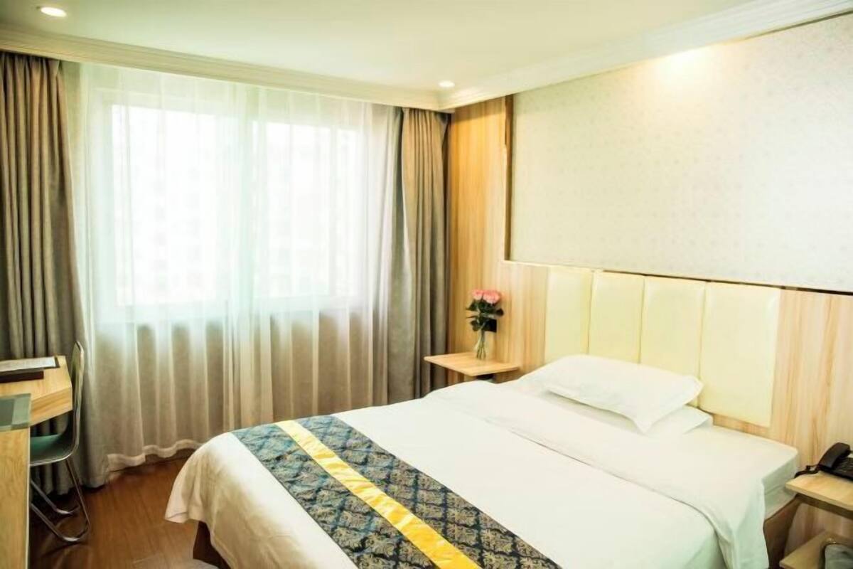 Une chambre d’hôtel avec un lit, un bureau, une chaise, une table de chevet et une fenêtre avec des rideaux.