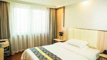 A hotel room with a bed, a desk, a chair, a nightstand, and a window with curtains.