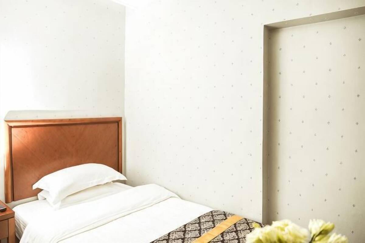 Une chambre d’hôtel avec une tête de lit en bois, un lit avec une literie blanche et un mur orné d’un motif discret.