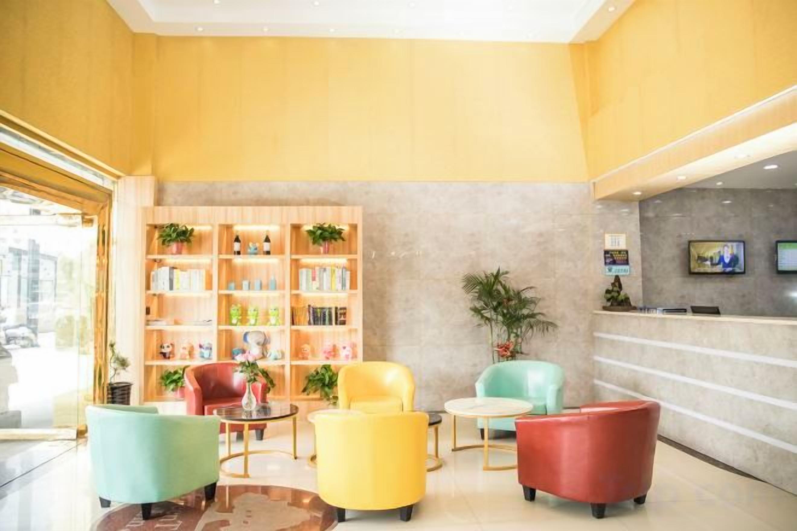 A hotel lobby with a reception desk, seating area with armchairs, and a bookshelf.