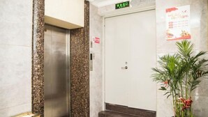 Un ascensor en el vestíbulo de un hotel, con una pared de mármol y una planta en maceta.