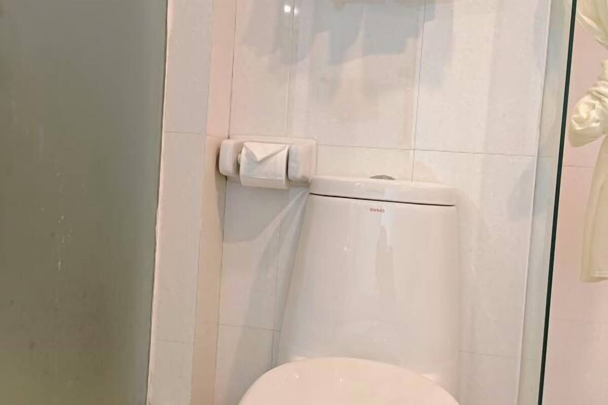 A bathroom with a toilet, a towel dispenser, and a glass shower enclosure.