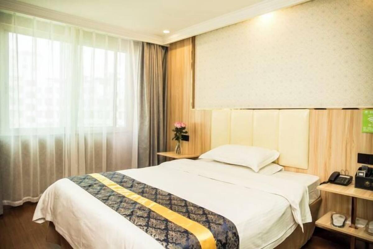Une chambre d’hôtel avec un grand lit, une table de chevet avec une lampe, un téléphone et un petit vase avec des fleurs.