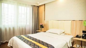 A hotel room with a large bed, a bedside table with a lamp, a telephone, and a small vase with flowers.