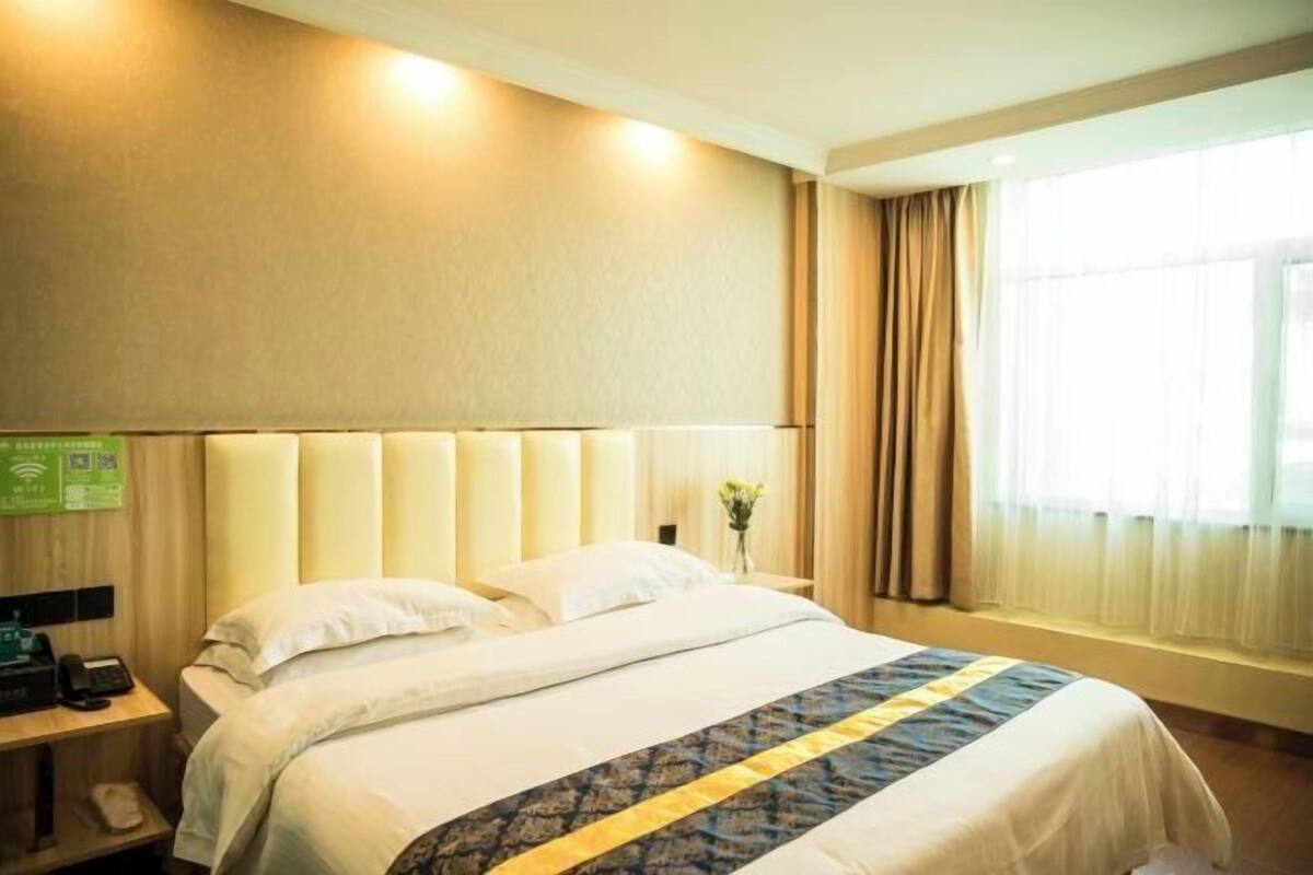 Une chambre d’hôtel avec un grand lit, une table de chevet avec une lampe et une fenêtre avec des rideaux.