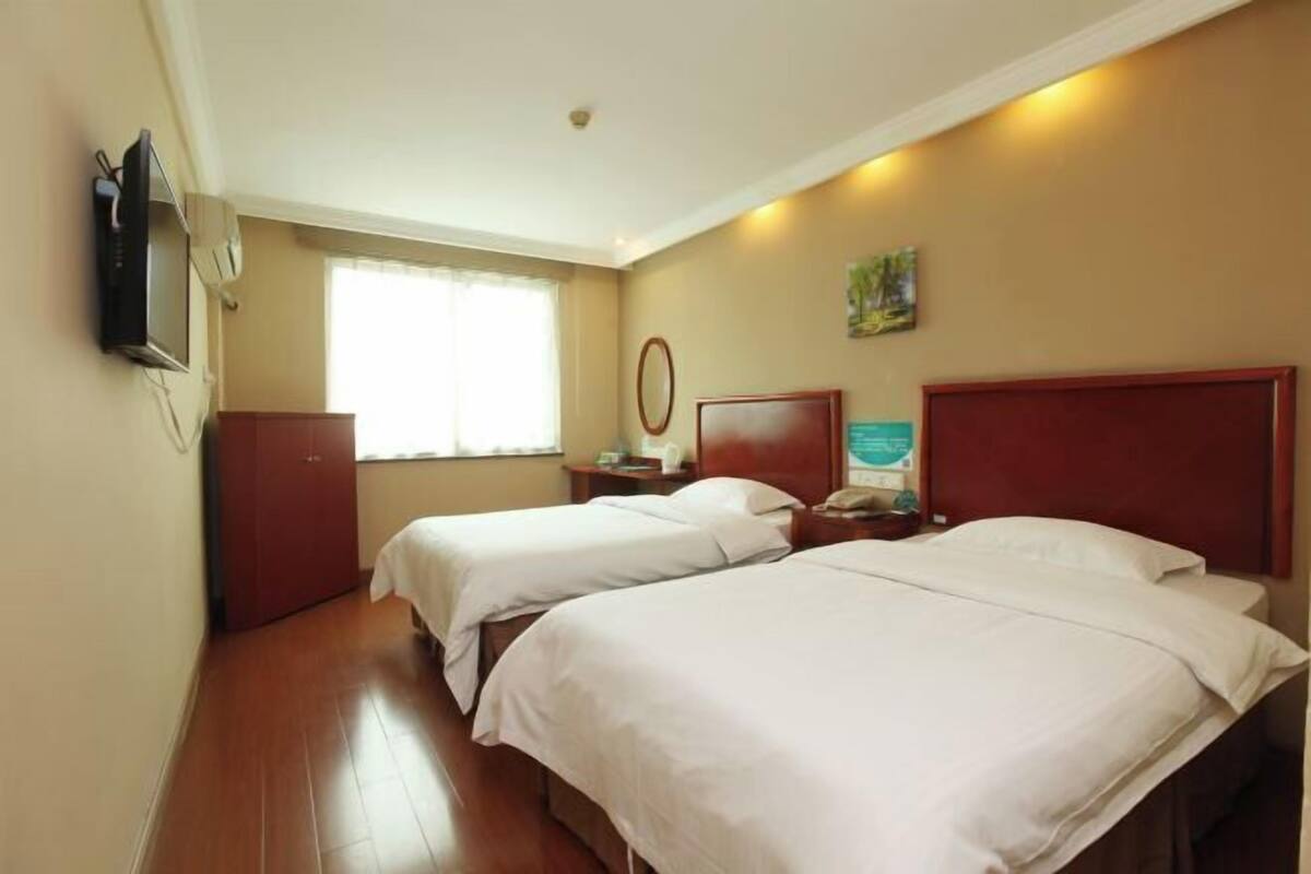 A hotel room with two beds, a television, a window with curtains, and a painting on the wall.