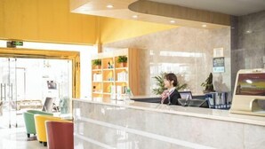 Zona de recepción de hotel con mostrador de mármol, sillas de colores y una estantería al fondo.