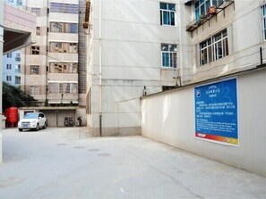Ein Parkplatz mit einem weißen Auto vor einem Gebäude mit vielen Fenstern und einem blauen Schild an der Wand.
