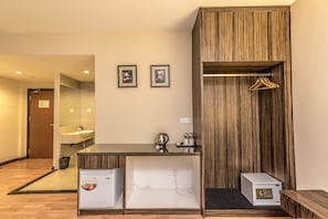 A compact room with a wooden vanity, a small refrigerator, a coffee maker, and a hanging clothes rack.
