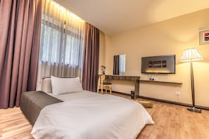 A hotel room with a bed, a desk, a TV, and a lamp.