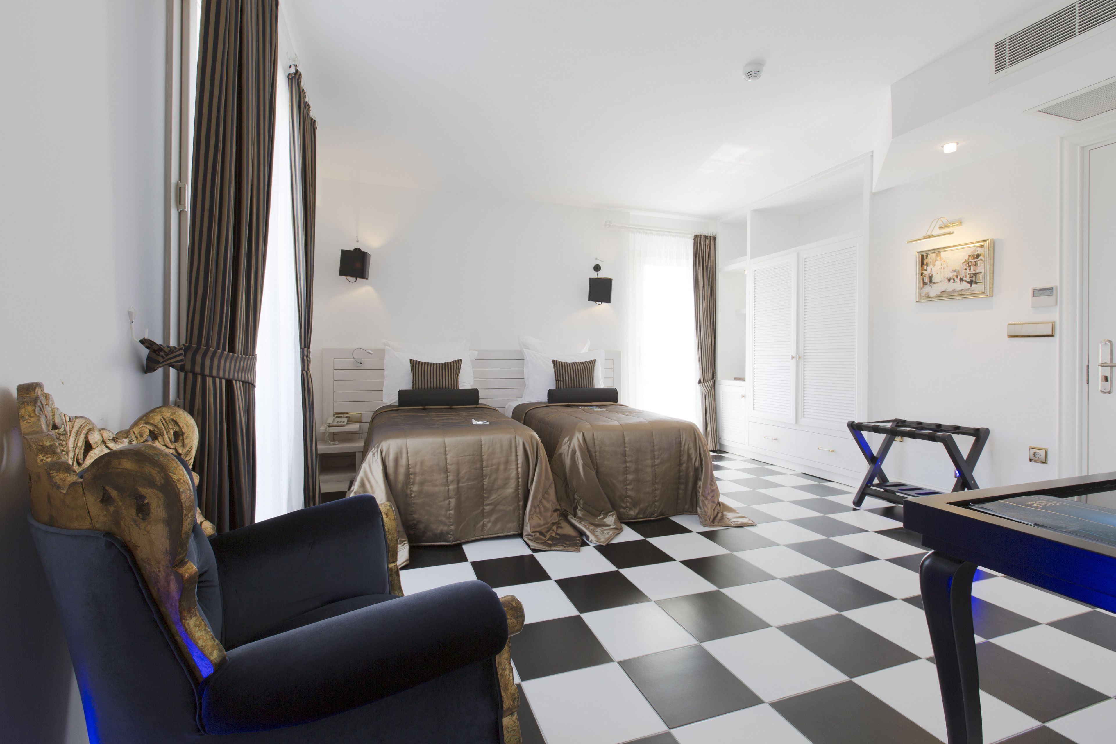 Habitación de hotel con piso a cuadros, dos camas, mesa de billar, sofá y un gran ventanal con cortinas.