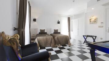 Habitación de hotel con piso a cuadros, dos camas, mesa de billar, sofá y un gran ventanal con cortinas.
