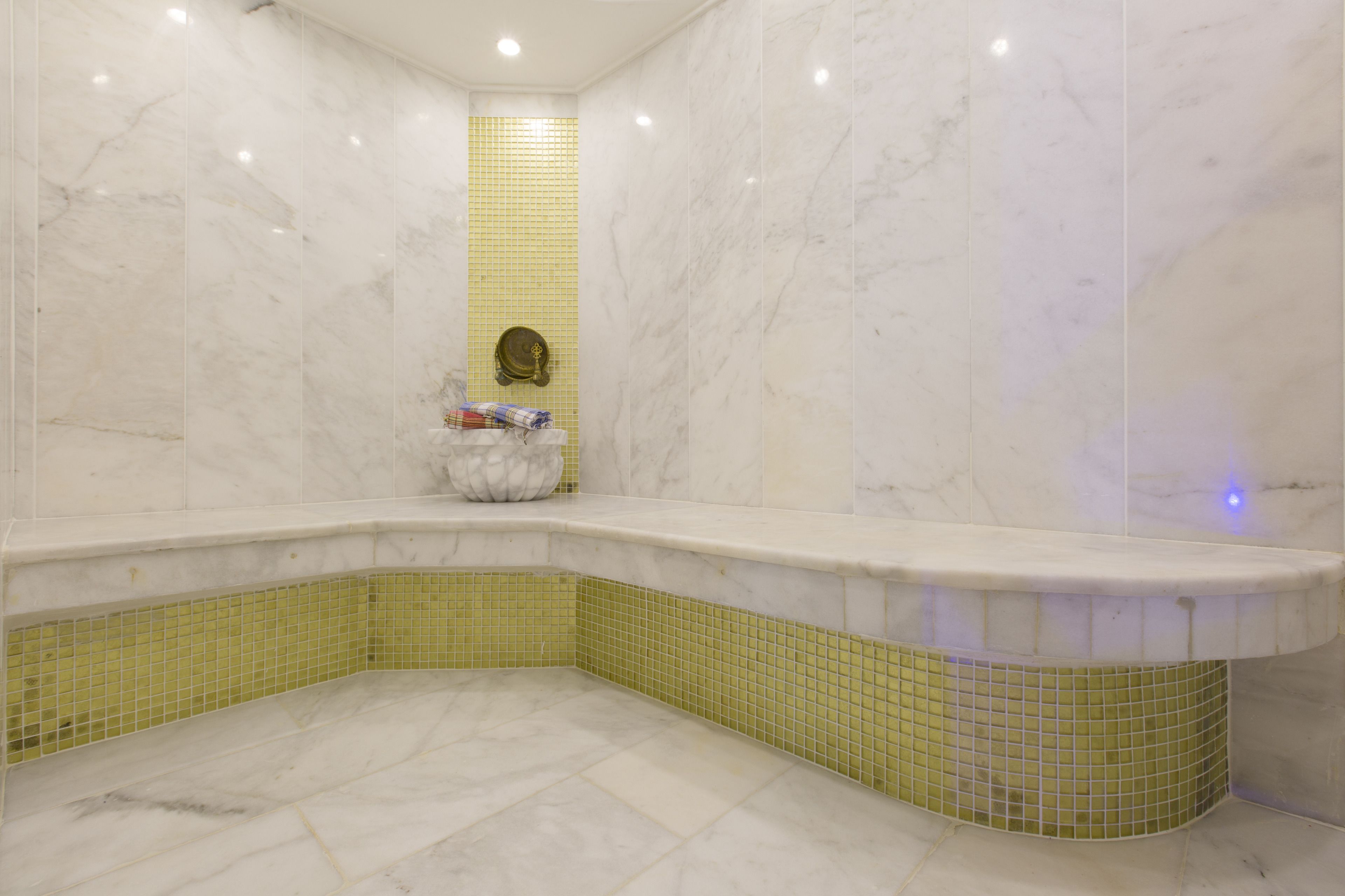 Ein Badezimmer mit einer Eckbadewanne, gelb gefliesten Wänden und einem Marmorboden.