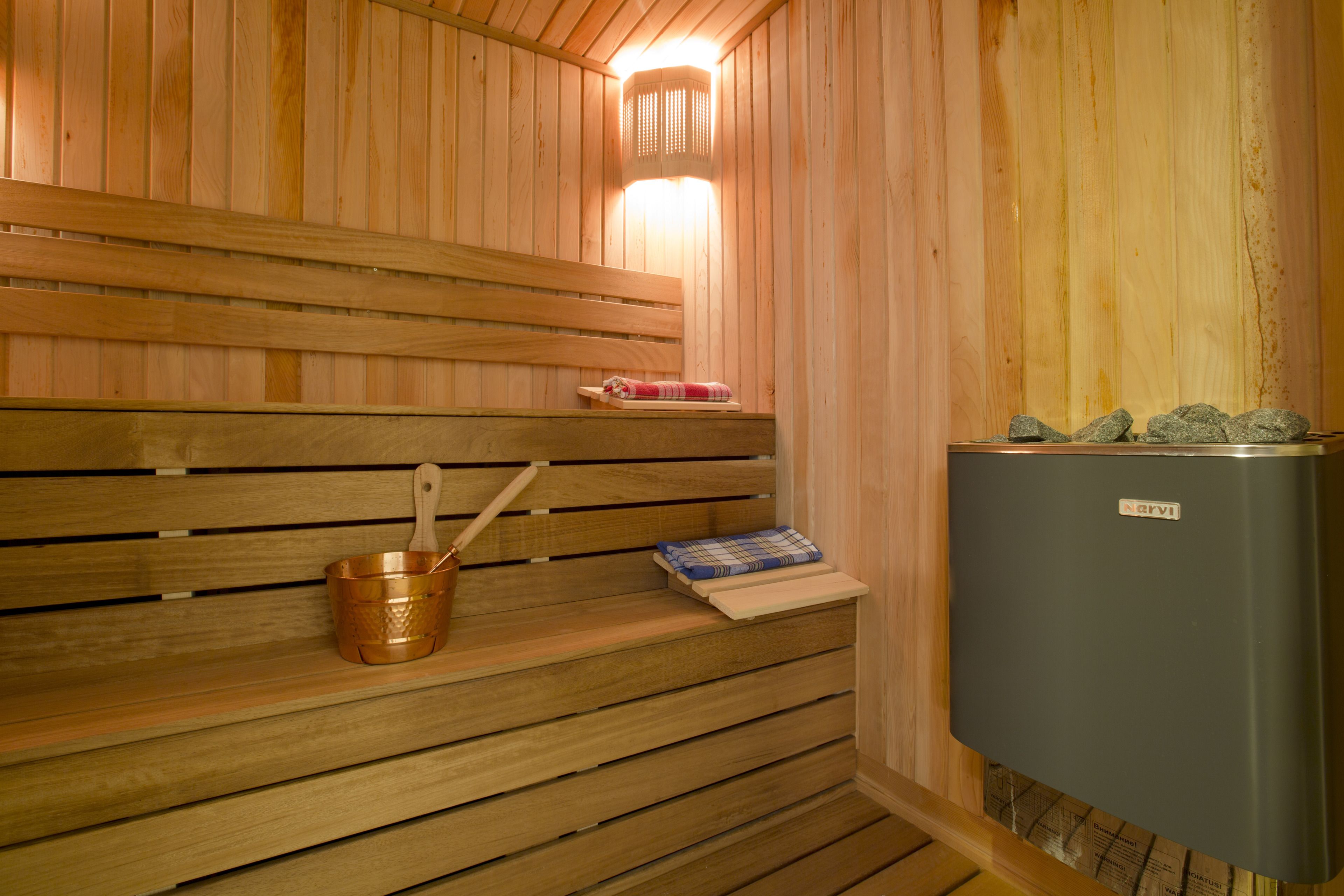 A sauna with wooden benches, a copper bucket, a towel, and a heater.