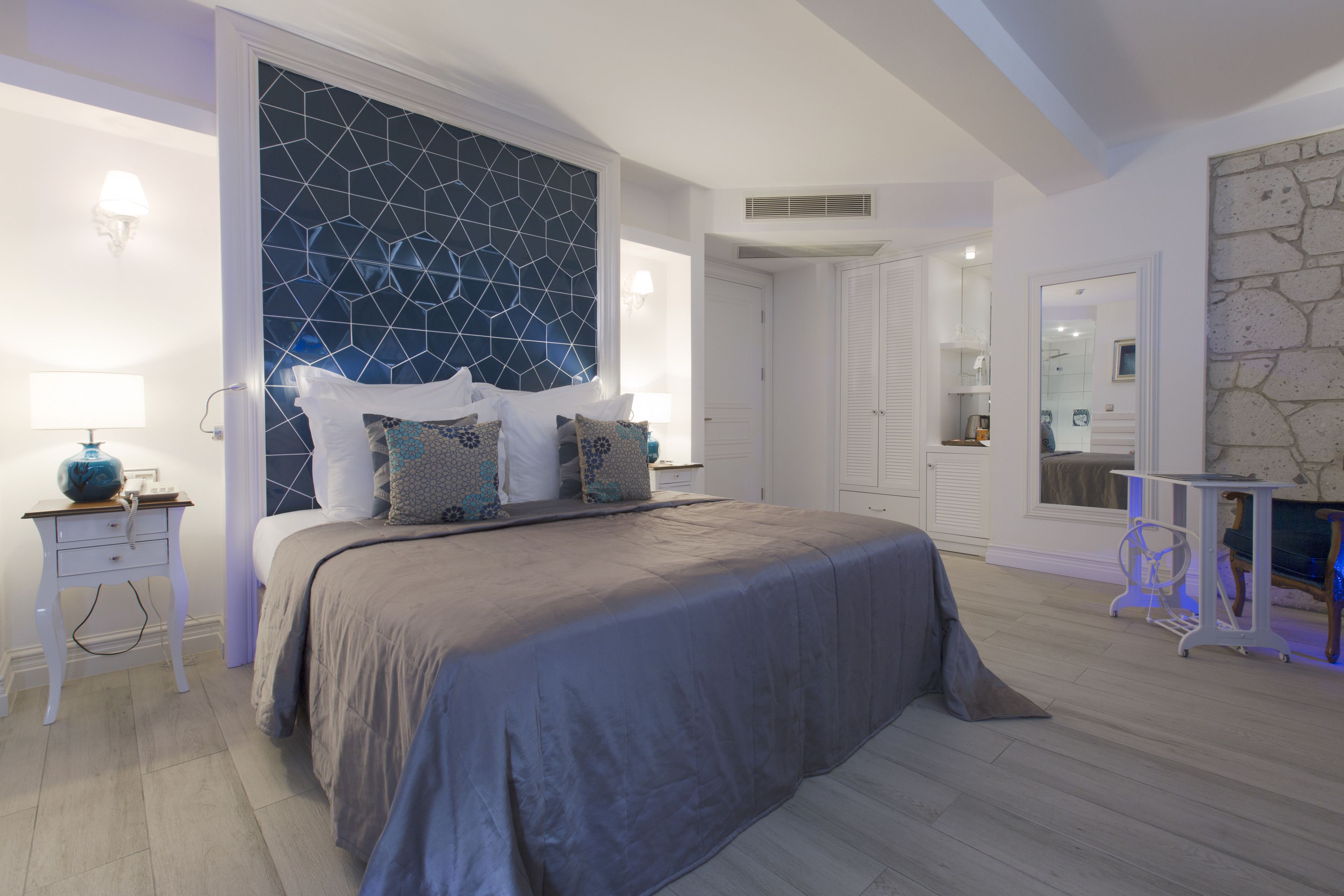 A bedroom with a large bed, a geometric-patterned headboard, a bedside table with a lamp, and a nightstand.