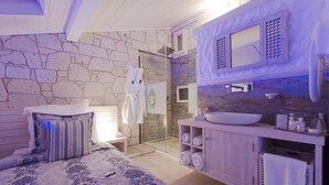 Un dormitorio con una cama grande, un baño con pared de piedra, ducha y tocador con lavabo.