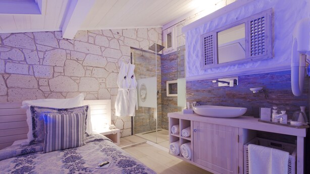 Un dormitorio con una cama grande, un baño con pared de piedra, ducha y tocador con lavabo.