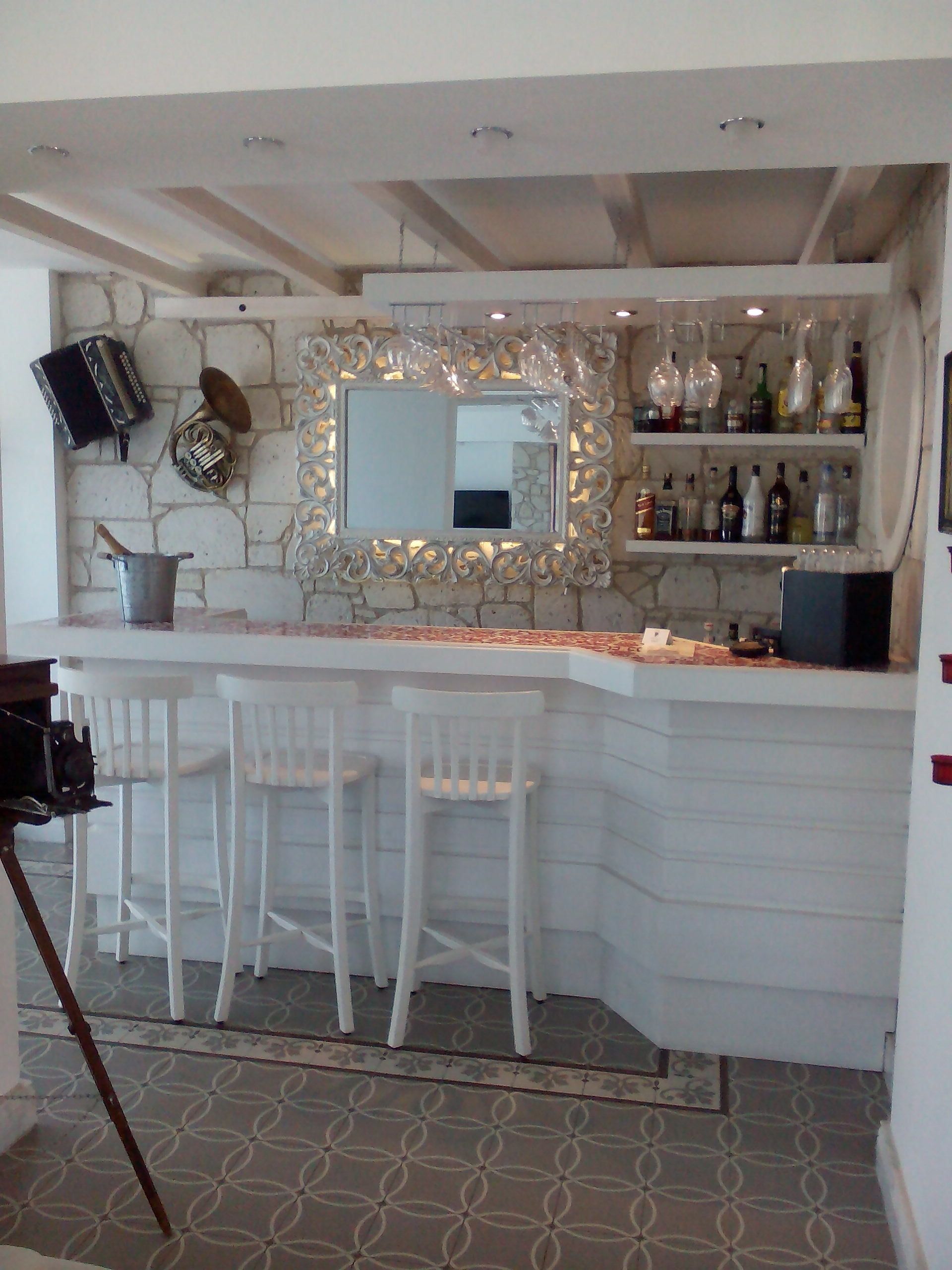 Una zona de bar con pared de piedra, un espejo decorativo y una estantería con botellas.