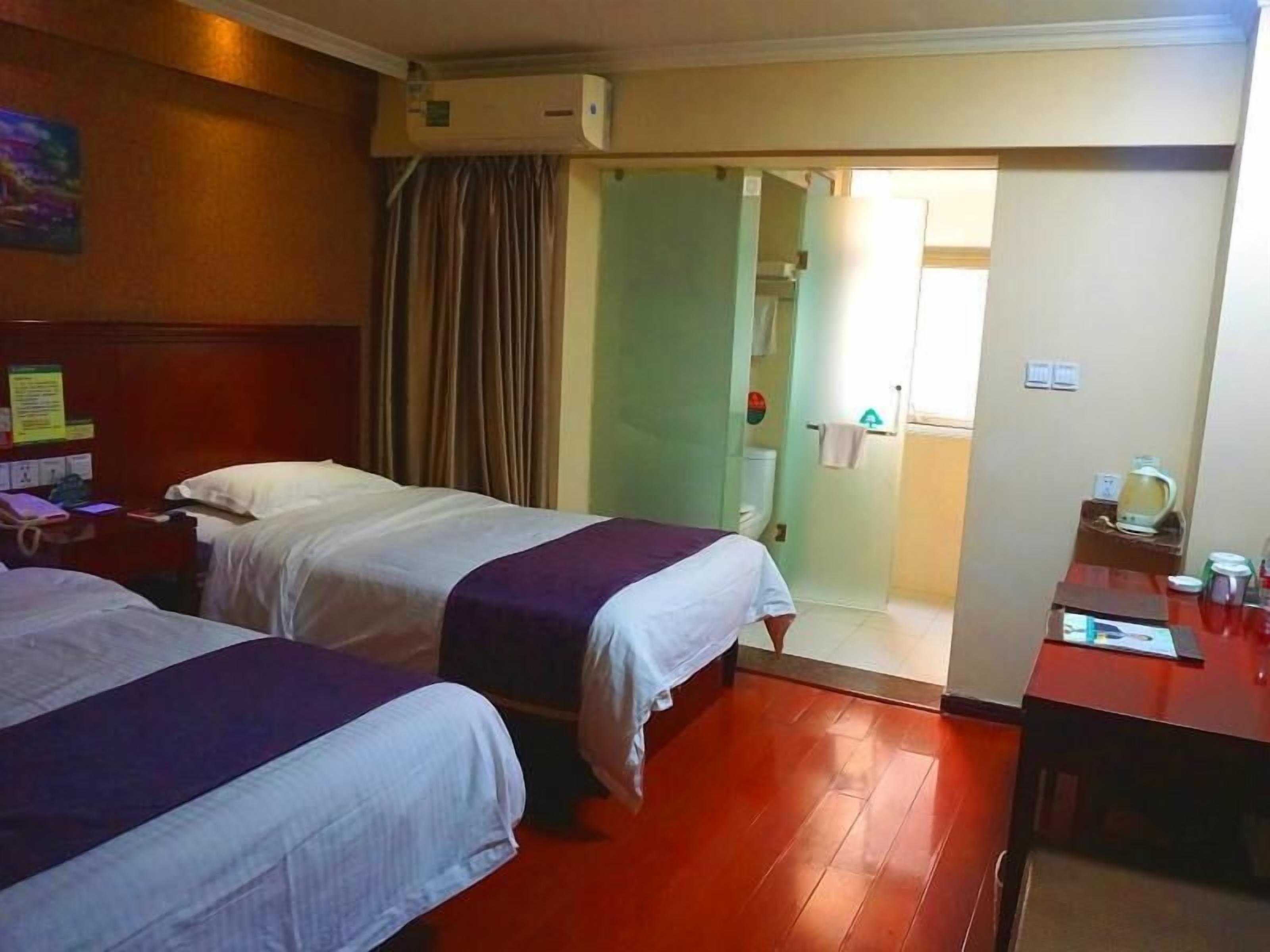 A hotel room with two beds, a desk, a chair, a coffee maker, and a bathroom visible through an open door.