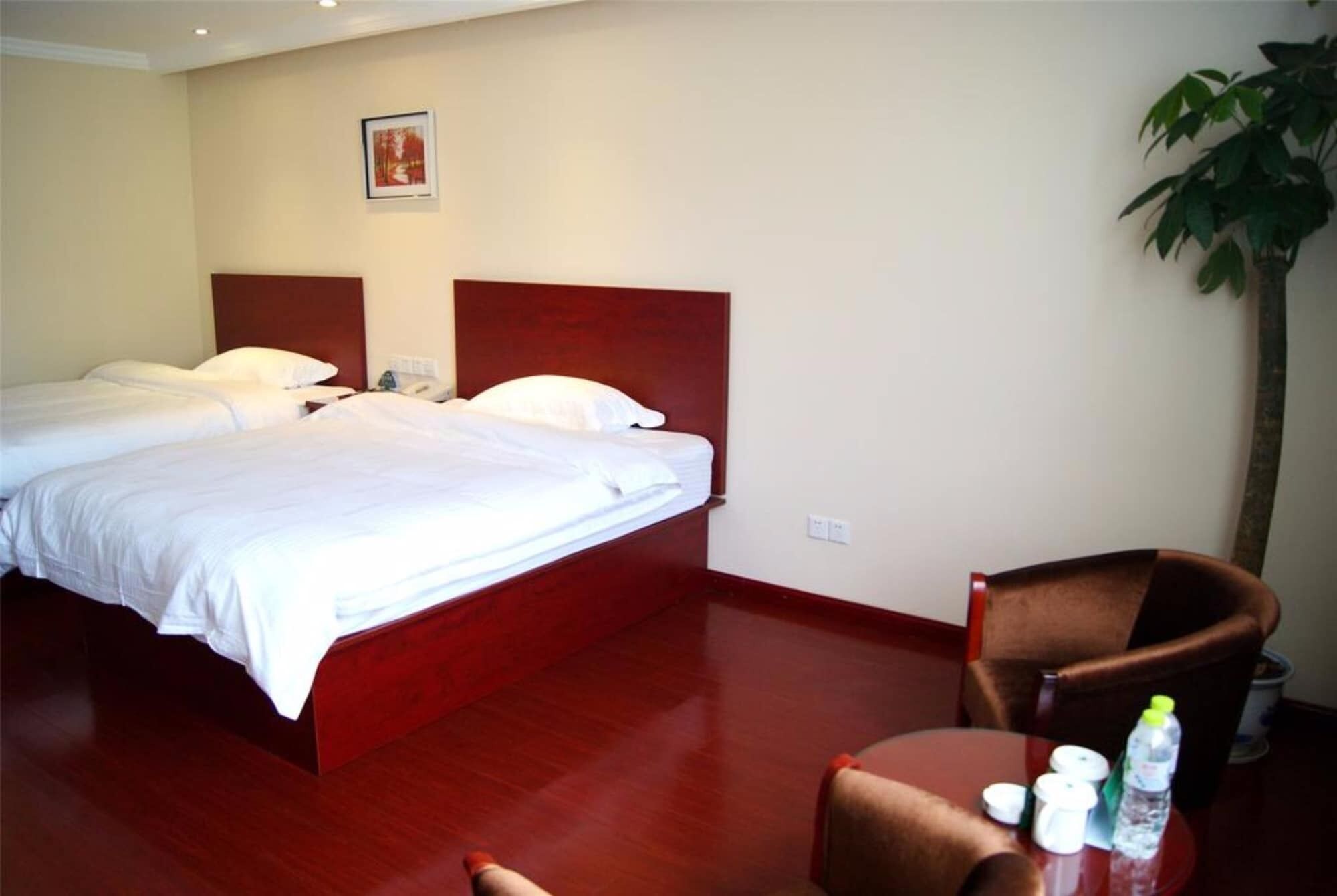 A hotel room with two beds, a wooden headboard, a small table with toiletries, and a potted plant.