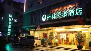 Un hotel con un letrero llamativo en caracteres chinos, una entrada bien iluminada y un estacionamiento con varios automóviles.
