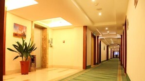 Un pasillo de hotel con alfombra de estampado verde, una planta en maceta y un cuadro en la pared.