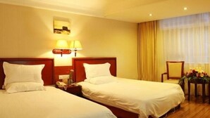 Una habitación de hotel con dos camas, una mesita de noche con lámpara, una silla y una ventana con cortinas.