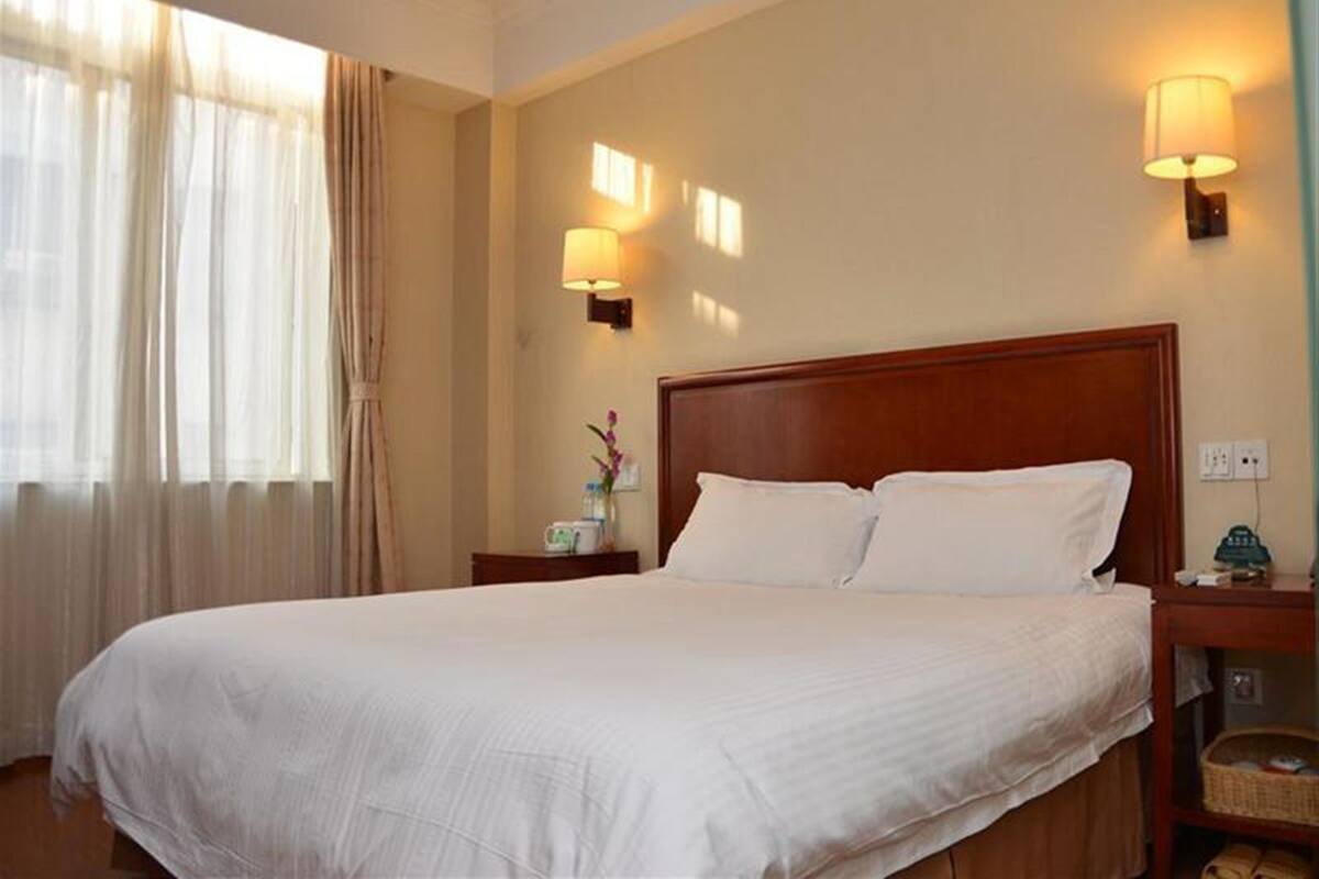 A hotel room with a large bed, two bedside lamps, a nightstand, and a window with curtains.