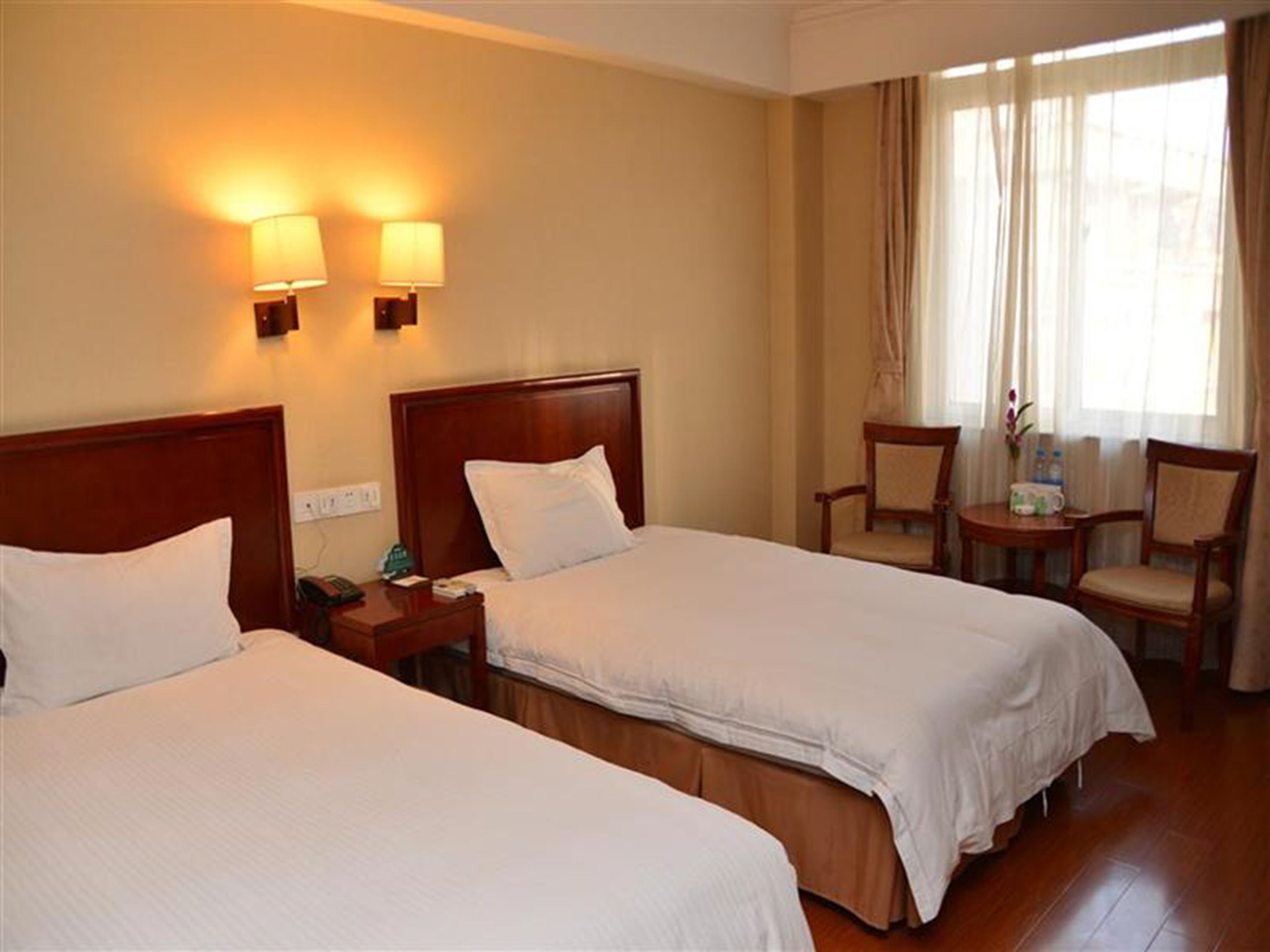 A hotel room with two beds, a nightstand with a phone, a chair, and a small table with a vase and water bottles.