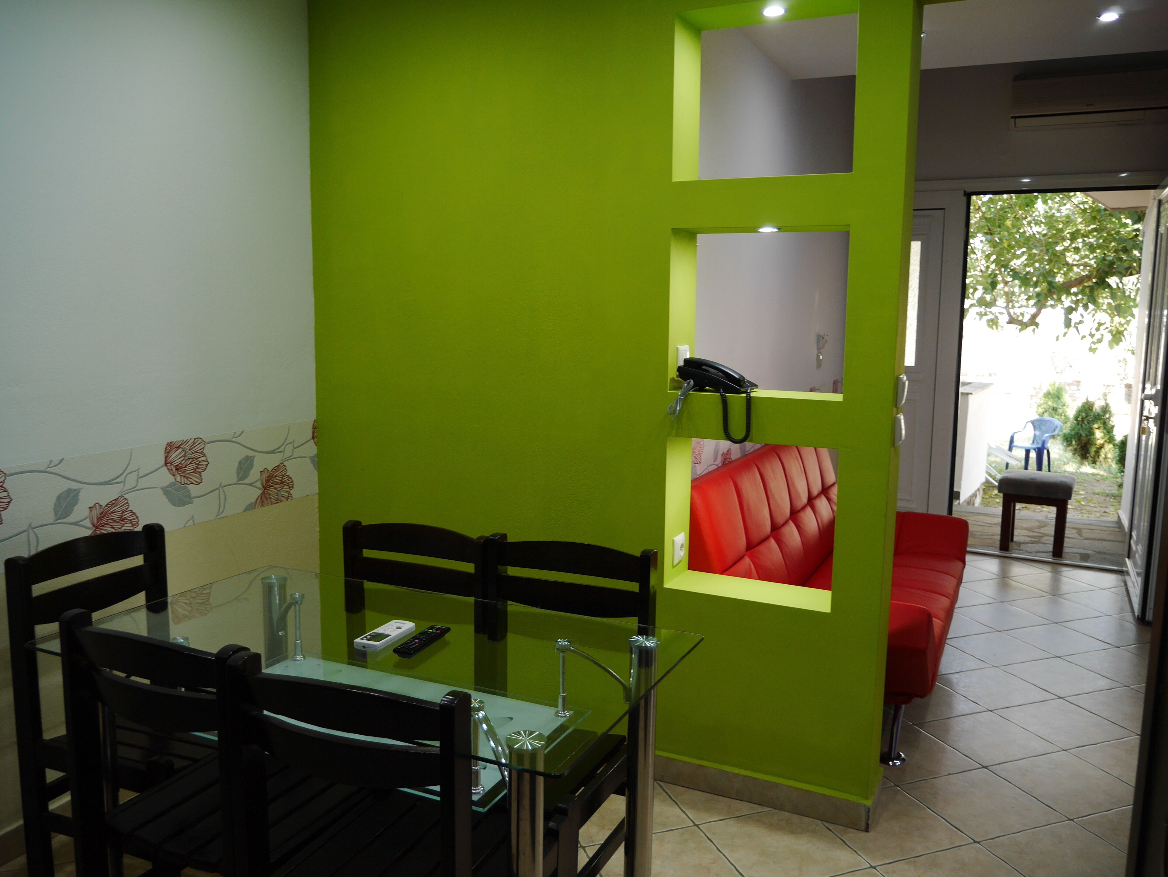A dining area with a green wall, a red cushioned bench, and a glass table with chairs.