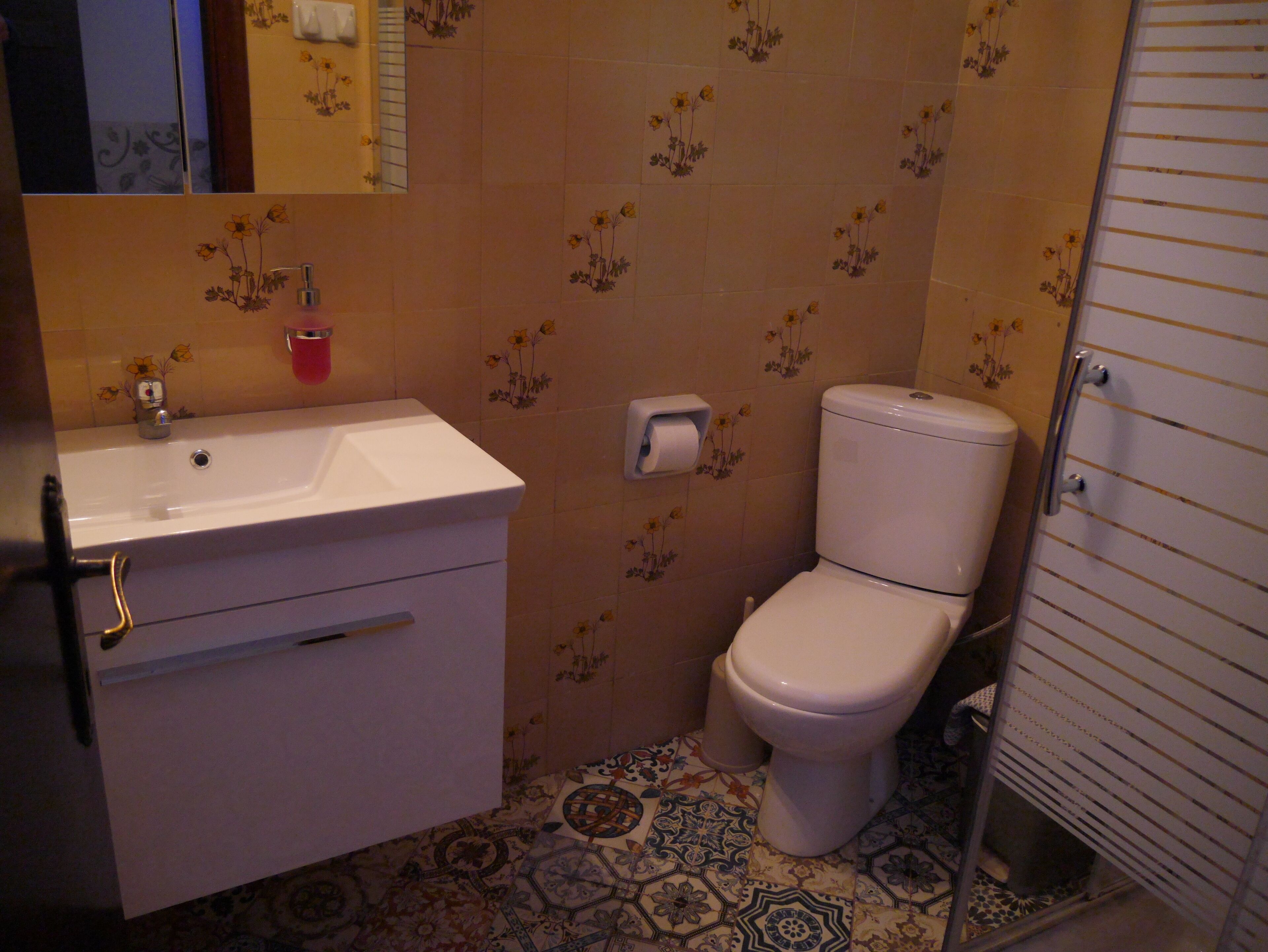Un baño con lavamanos, inodoro y baldosas de suelo estampadas.