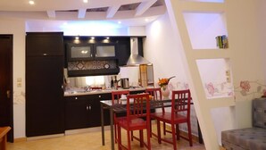 A modern kitchen with dark cabinetry, a central island, and a dining area with red chairs. - Blue Sky Apartments (Thasos)