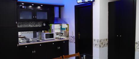A modern kitchen with dark cabinetry, a glass dining table, and a television mounted above the counter.