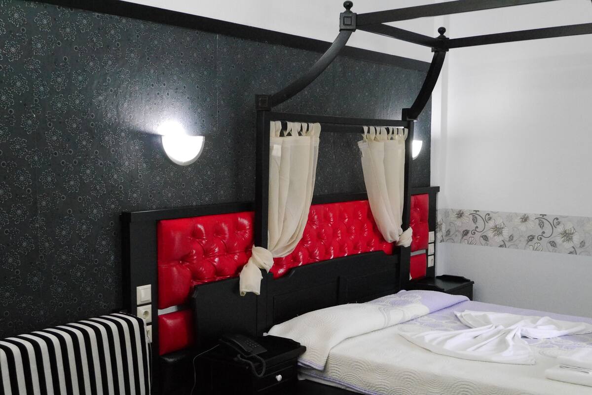 A hotel room with a black and red headboard, a striped sofa, a bed with white bedding, and a bedside table with a phone.