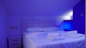 A bedroom with a bed, white bedding, a nightstand, and a blue wall. - Blue Sky Apartments (Thasos)