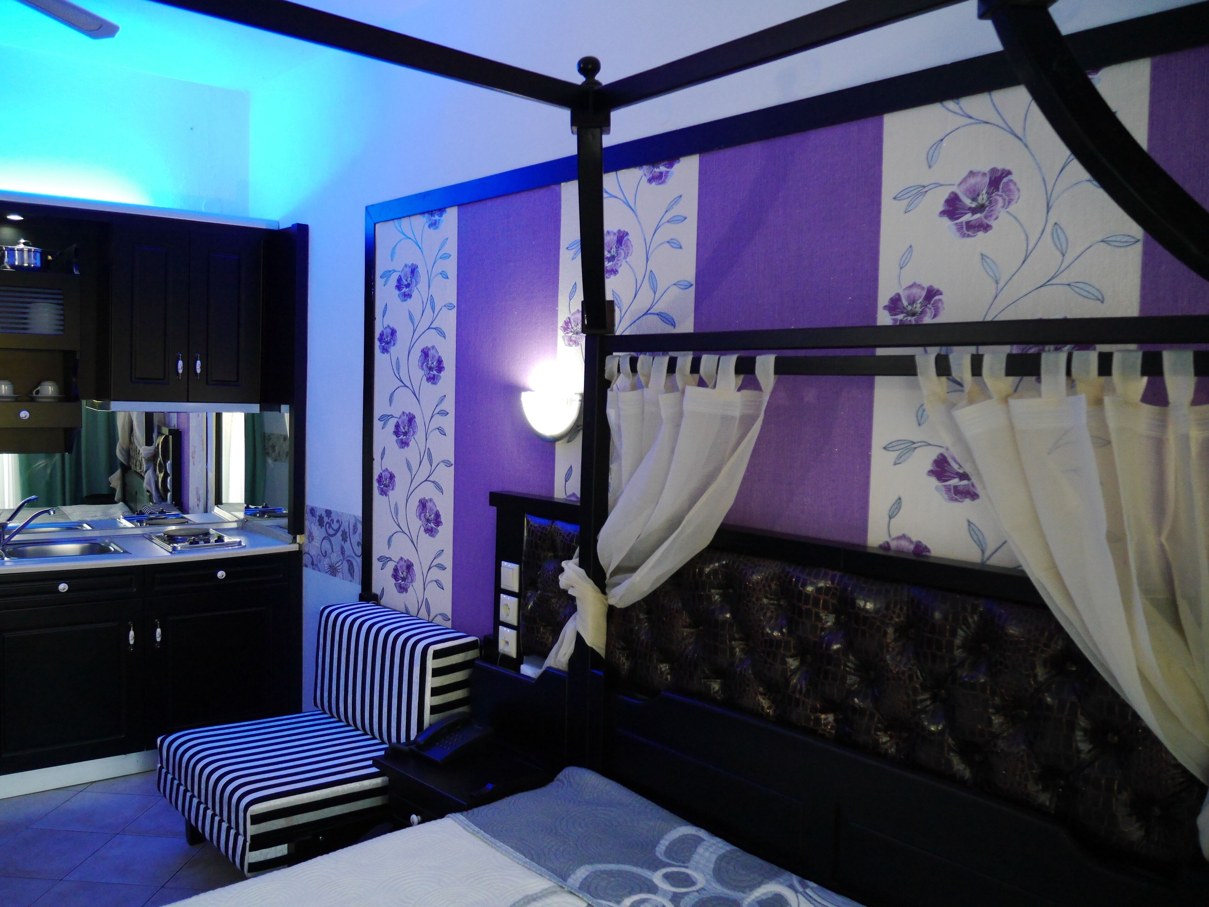 A bedroom with a four-poster bed, a small bedside table, a chair, and a built-in wardrobe.