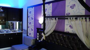 A bedroom with a four-poster bed, a small bedside table, a chair, and a built-in wardrobe.