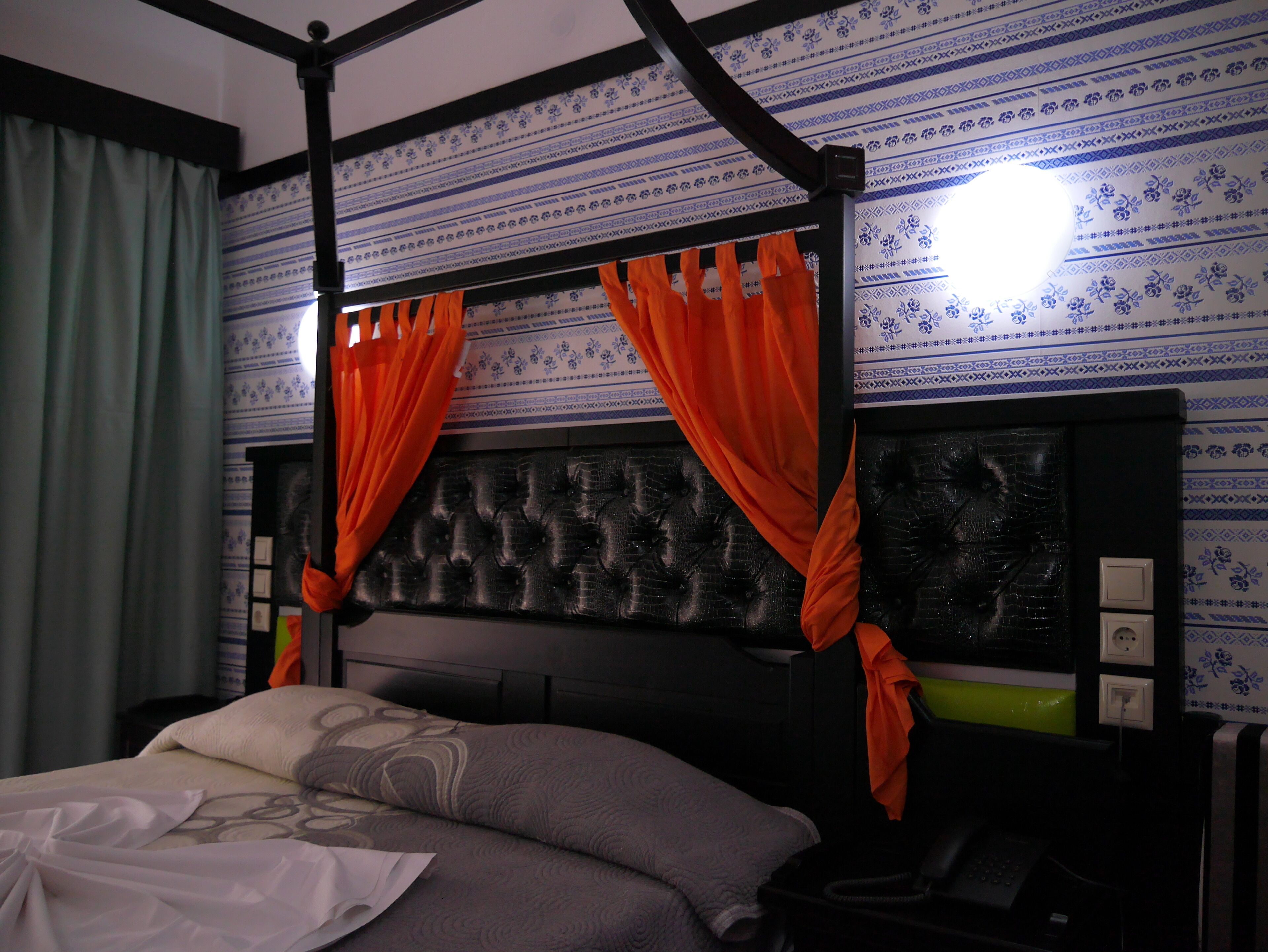 A bedroom with a four-poster bed, a tufted headboard, and patterned wallpaper.