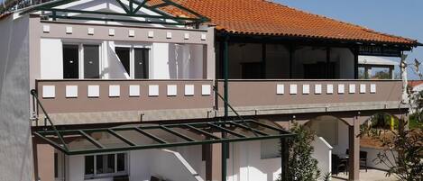 Um edifício de dois andares com terraço e área de estar coberta ao ar livre.