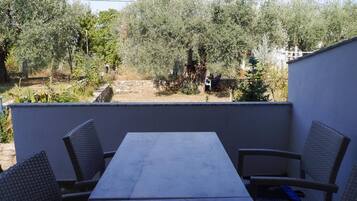 Patio esterno con tavolo in marmo e sedie in vimini, circondato da ulivi e un muro in pietra.