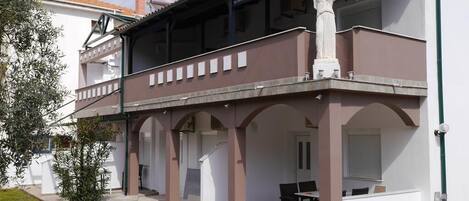 Ein zweistöckiges Gebäude mit Balkon, Sitzgelegenheiten im Freien und einer Statue.
