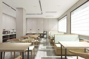 Un interior moderno con mesas y sillas dispuestas para comer, una encimera con electrodomésticos de cocina y amplios ventanales que dejan entrar luz natural.