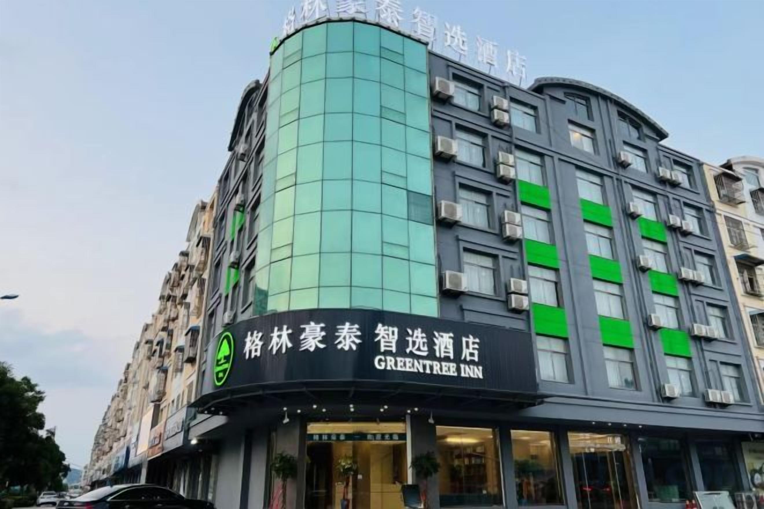A hotel building with a curved facade, a prominent green-lit corner, and signage for the GreenTree Inn.